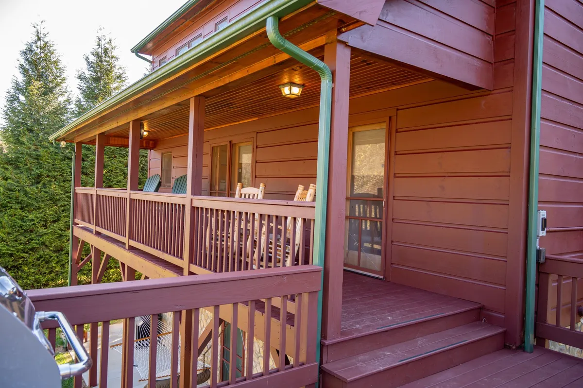 This photo highlights two wooden rocking chairs on a charming front porch, surrounded by greenery. The setting conveys a sense of tranquility, perfect for stargazing, socializing, or unwinding in the fresh mountain air.