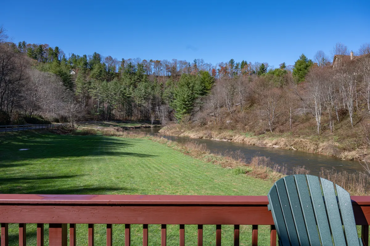 A peaceful, scenic view of the lawn leading down to the river, framed by a deck chair that faces the water. The forested edge and gentle flow of the river evoke relaxation, nature-watching, and quiet moments after a day of adventure.