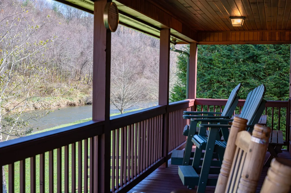 This image captures a tranquil exterior view from a porch with rocking chairs overlooking a serene river, set against a backdrop of lush greenery and natural surroundings. It invites viewers to imagine unwinding while immersed in nature, with the water and trees highlighting the region's scenic beauty.