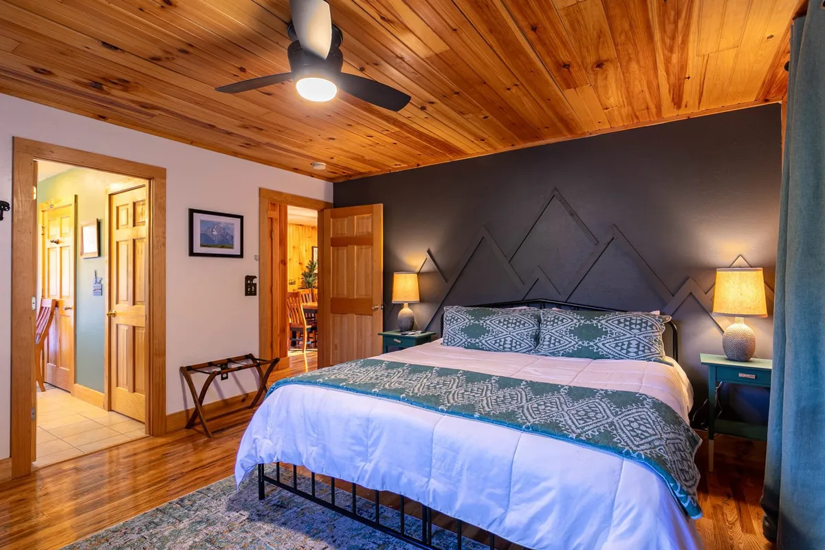 This image features a bed with patterned bedding set beneath a wooden ceiling, flanked by nightstands with lamps that emit a warm, soft glow. The scene is inviting and serene, emphasizing comfort and tranquility—key elements in a restful retreat.