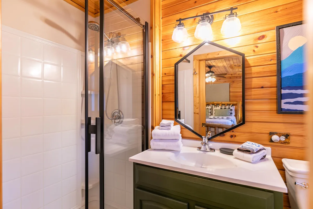 A serene bathroom with wood paneling, a shower area, vanity with sink, and bright lighting fixtures. The room feels calm and comfortable, creating a space for relaxation and personal care after a busy day.