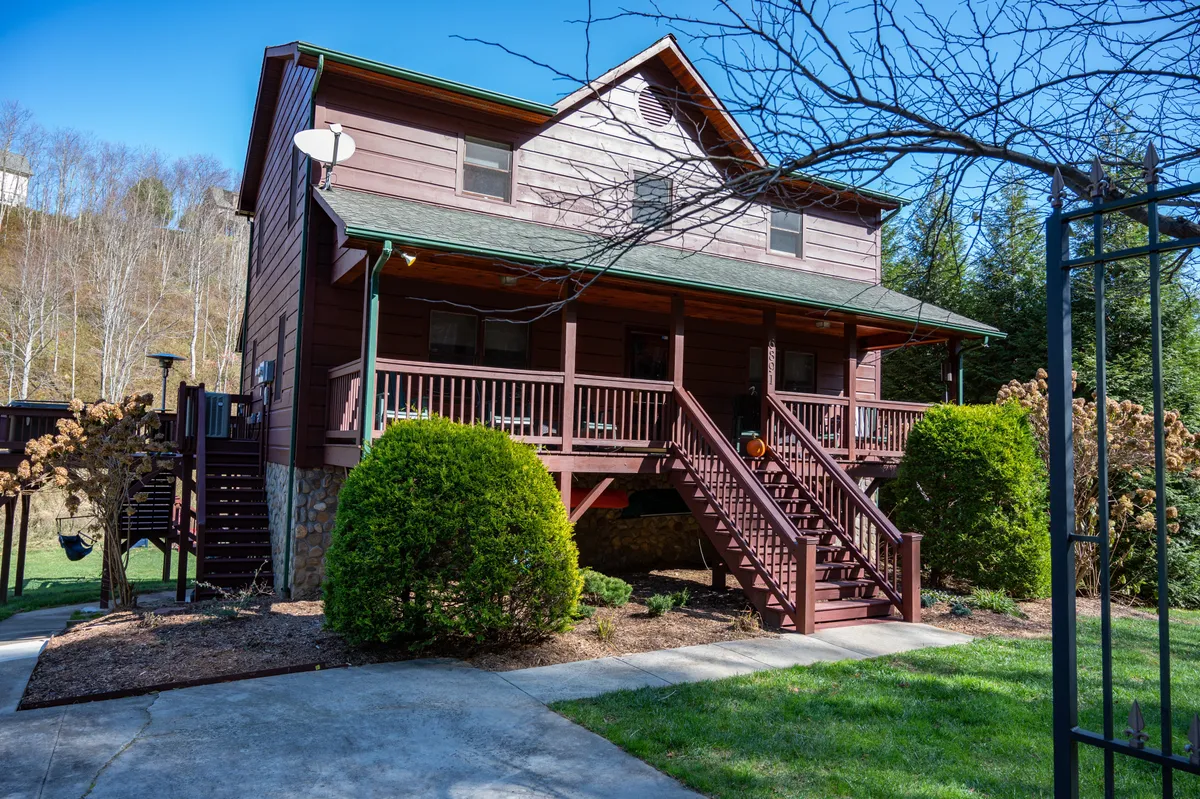 This image captures the exterior of the Riverbend Retreat, featuring a welcoming wooden deck, the front entrance, a landscaped garden, and the staircase. The inviting porch and lush outdoor setting suggest a perfect spot for relaxing after a day of mountain adventures or gathering with friends and family for evening barbecues.