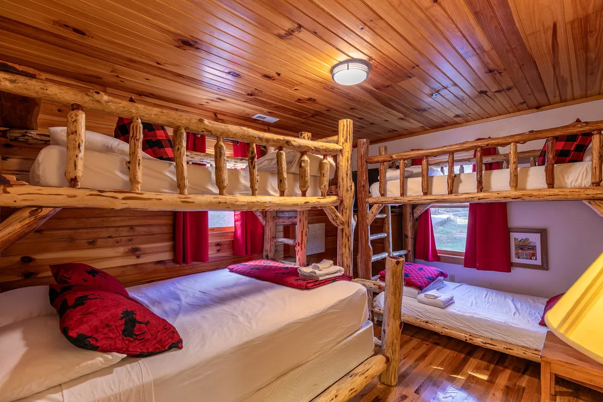 A playful, inviting bunk room with custom-built wooden bunk beds, colorful bedding, and cheerful red curtains. The space feels fun and welcoming, ideal for kids or the young-at-heart, radiating rustic mountain charm.