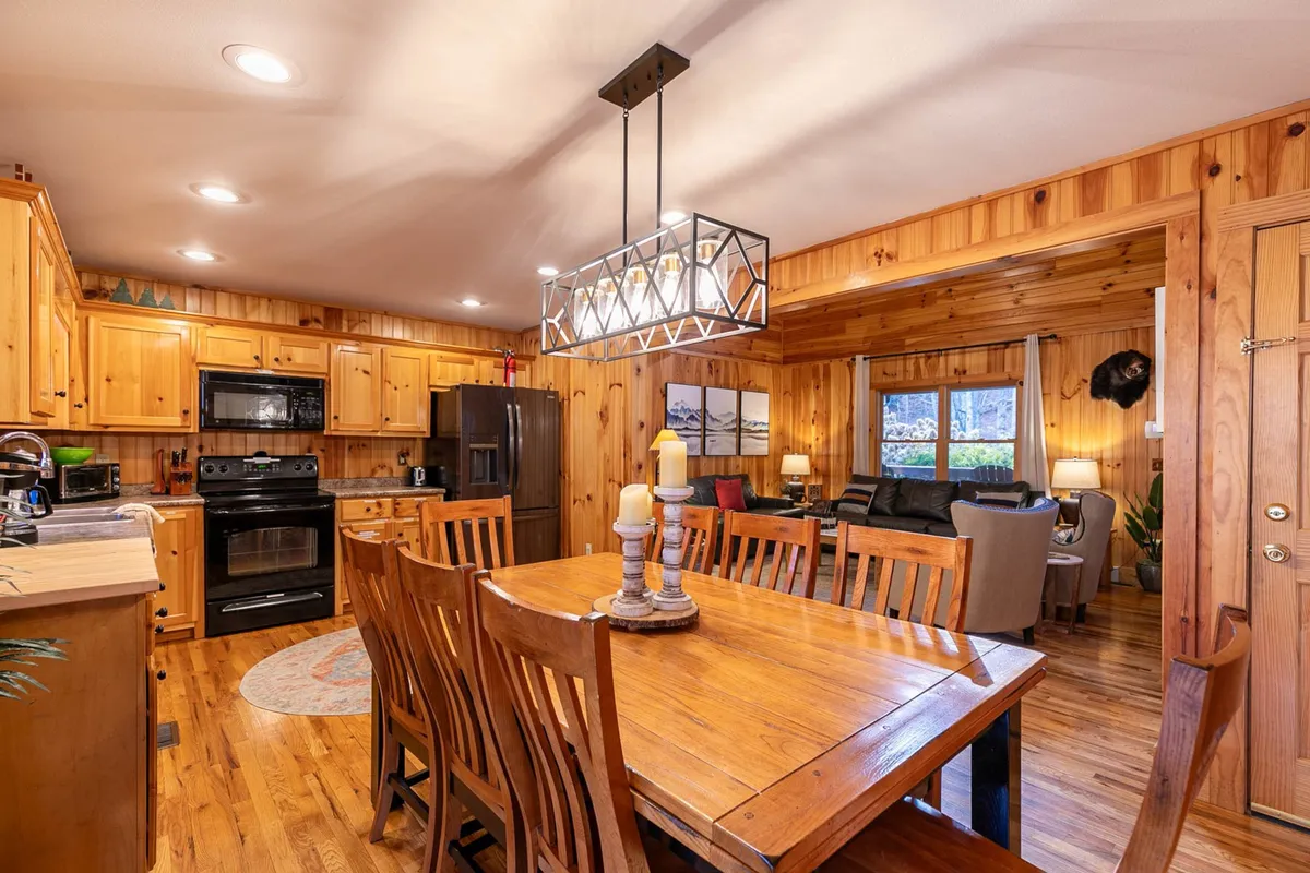 A warm, inviting dining space with a wooden dining table set for six, adjacent to the kitchen cabinetry and featuring a view into the living area. Soft lighting and cozy details create a homely atmosphere ideal for shared meals or game nights.